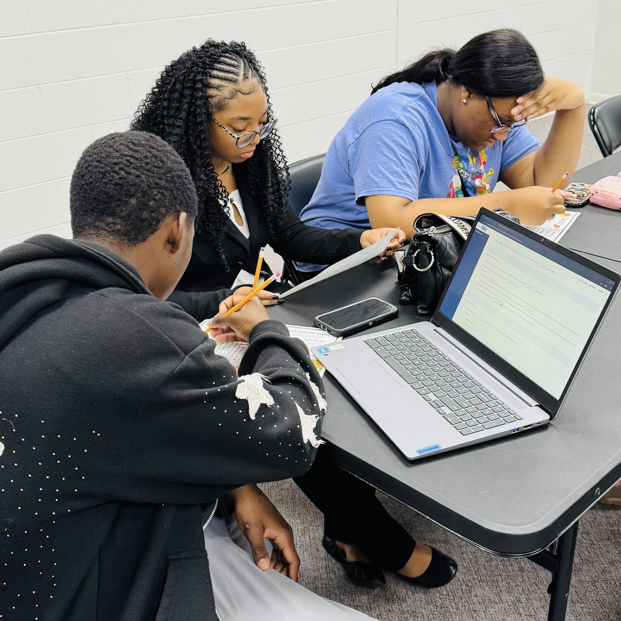 Three teens at a table with a laptop.
